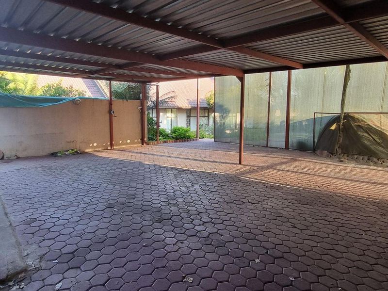 A spacious covered carport area featuring a metal roof structure and paved flooring, providing ample space for vehicle parking.