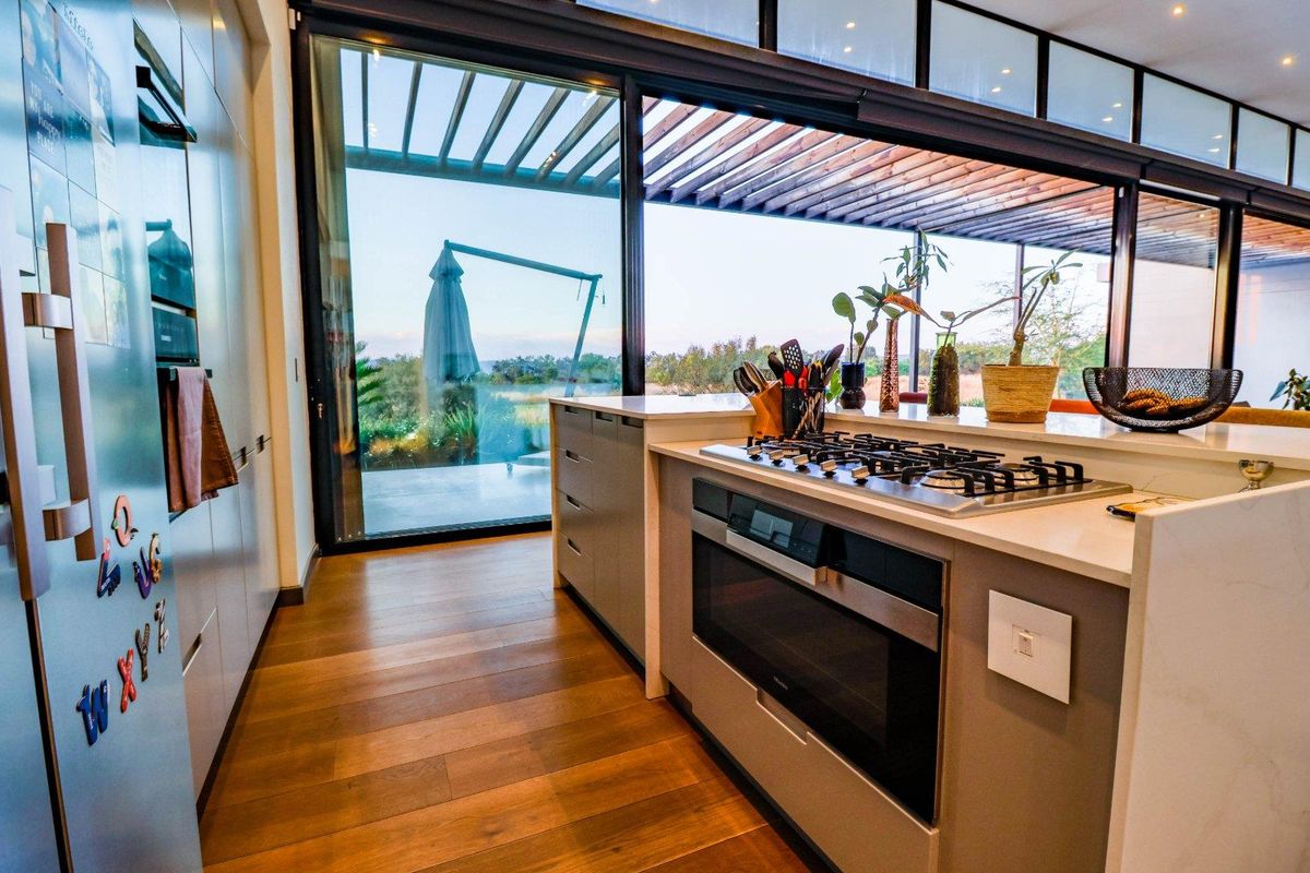 Modern kitchen featuring stone countertops, integrated gas cooktop and oven, hardwood flooring, and large sliding glass doors opening to an outdoor patio area.
