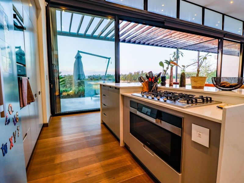 Modern kitchen featuring stone countertops, integrated gas cooktop and oven, hardwood flooring, and large sliding glass doors opening to an outdoor patio area.