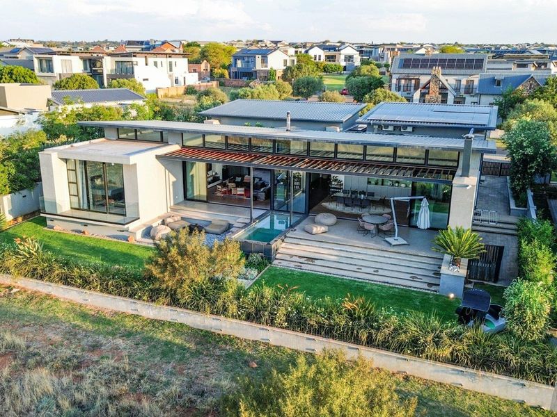 Aerial view of a modern contemporary residence featuring a metal roof, expansive sliding glass doors, a covered patio, and a private plunge pool.