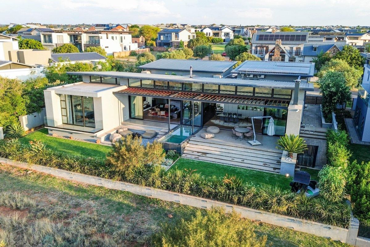 Aerial view of a modern contemporary residence featuring a metal roof, expansive sliding glass doors, a covered patio, and a private plunge pool.