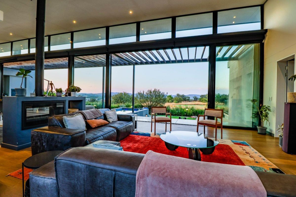 Spacious modern living room featuring a built-in fireplace and expansive floor-to-ceiling glass doors that open to a scenic outdoor patio and garden area.