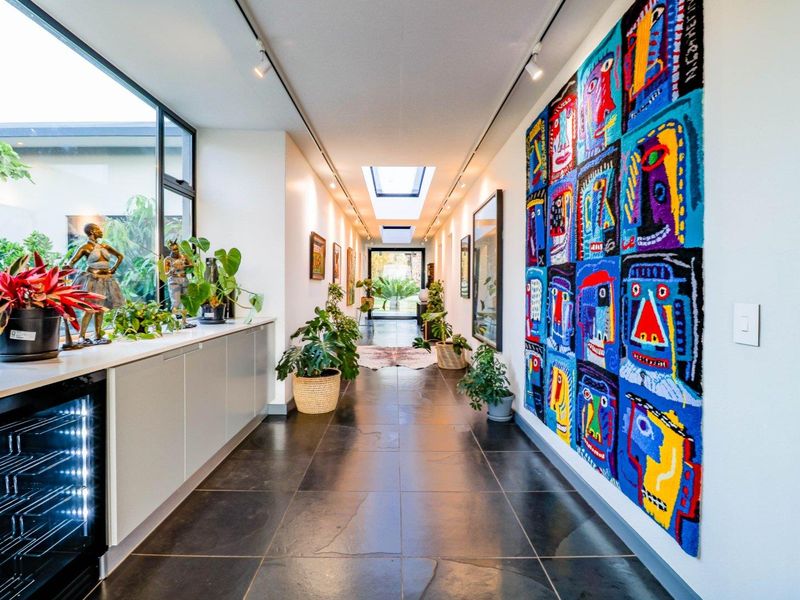 A bright, modern hallway featuring stone tile flooring, built-in cabinetry, track lighting, and a skylight, creating an airy and well-lit transition space.