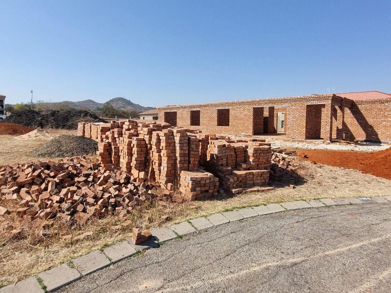 A residential construction site featuring a partially built brick structure with piles of building materials on the vacant land.