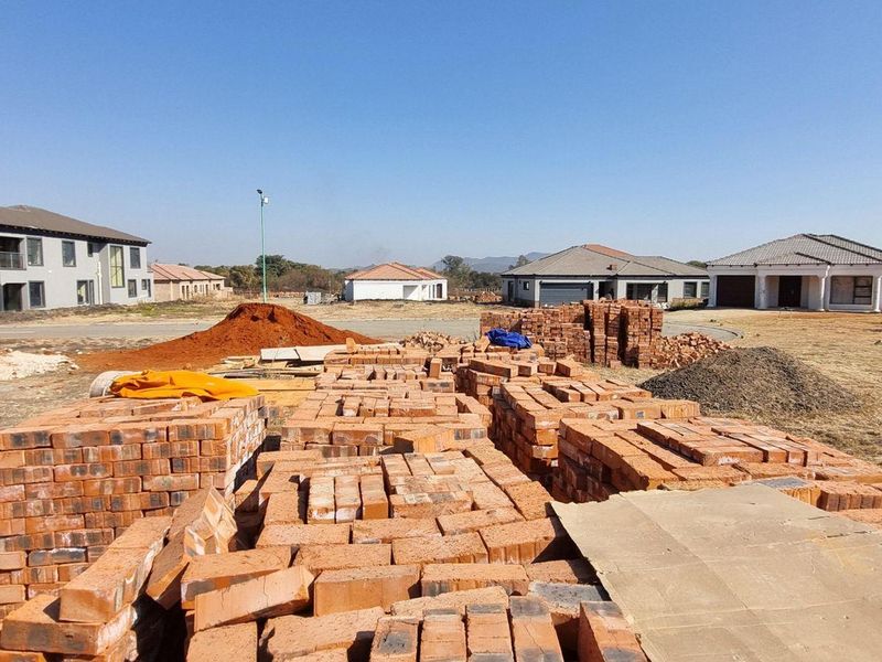 A vacant residential plot under development, featuring stacks of bricks and construction materials with surrounding neighborhood homes visible.