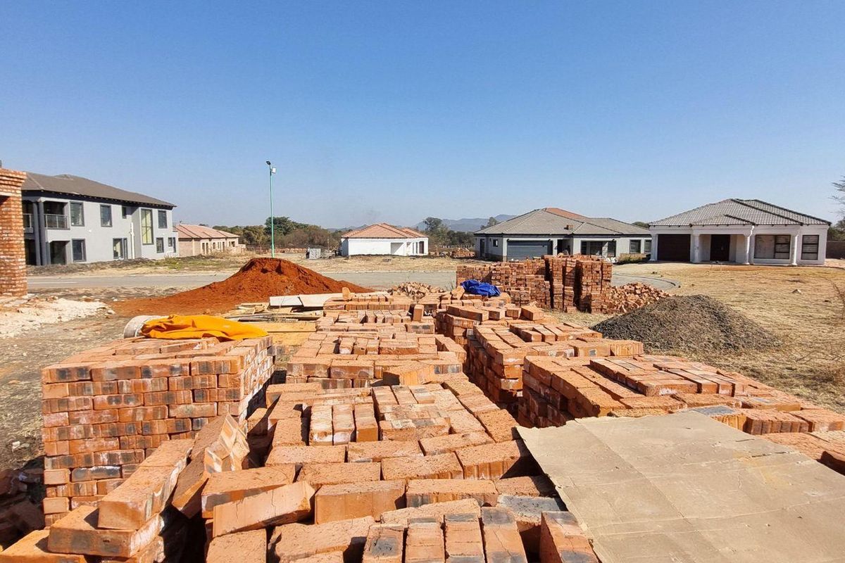 A vacant residential plot under development, featuring stacks of bricks and construction materials with surrounding neighborhood homes visible.