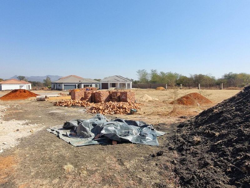 A view of a residential construction site featuring exposed brickwork, piles of building materials, and surrounding neighborhood development.