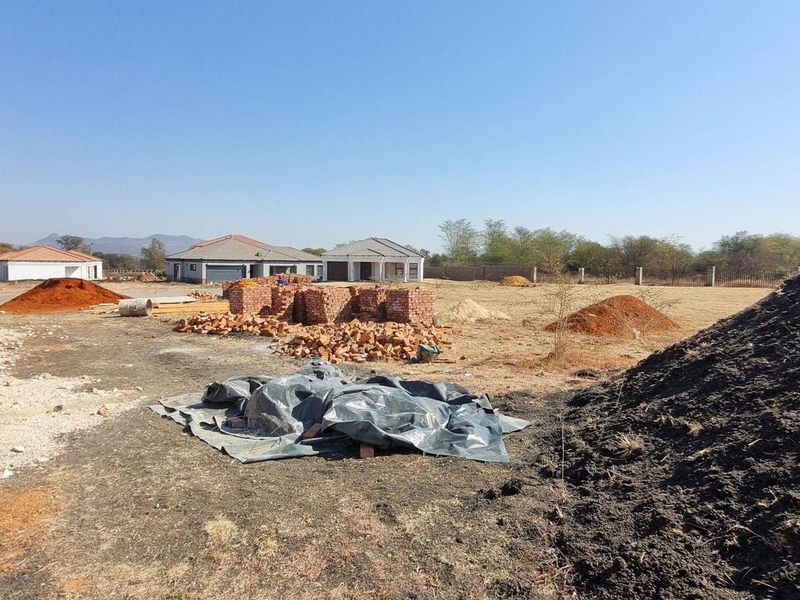 A view of a residential vacant land plot under development with piles of building materials and an unfinished brick structure.