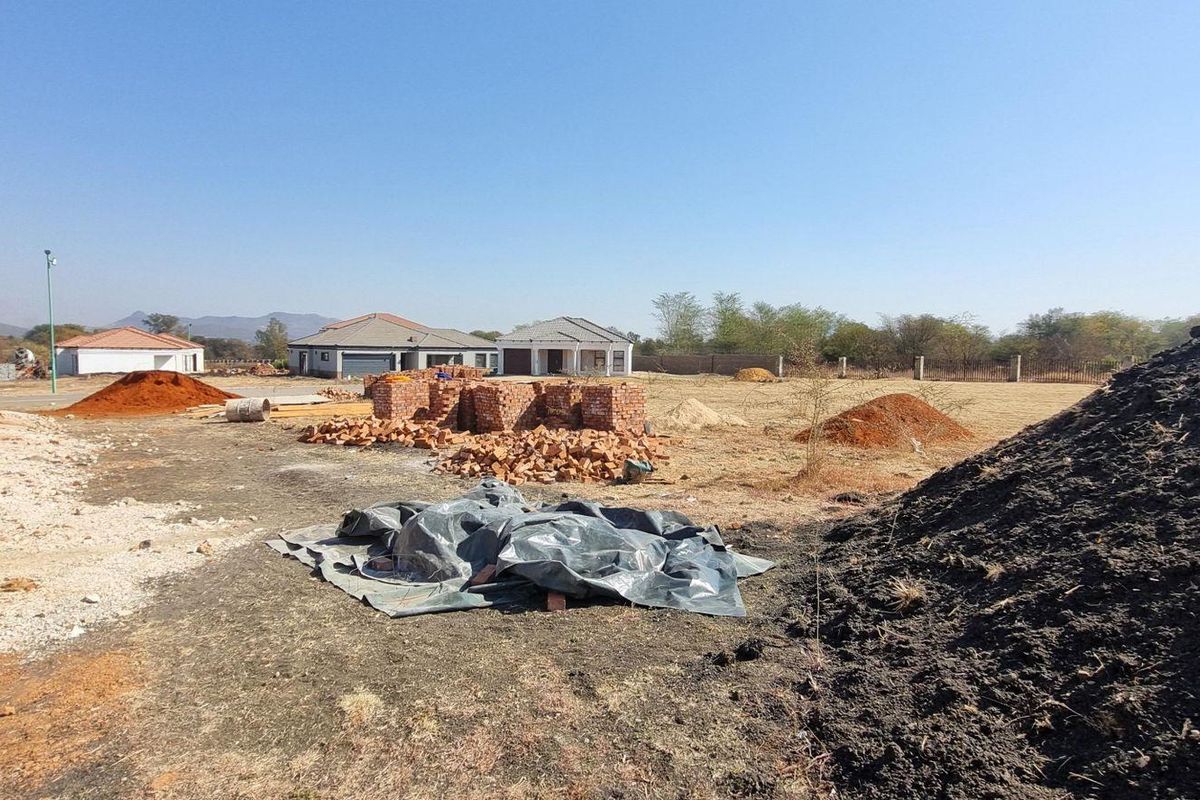 A view of a residential vacant land plot under development with piles of building materials and an unfinished brick structure.