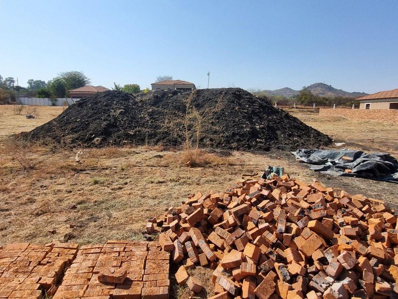 A view of a vacant residential plot featuring piles of soil and loose bricks, indicating ongoing site preparation or construction activity.