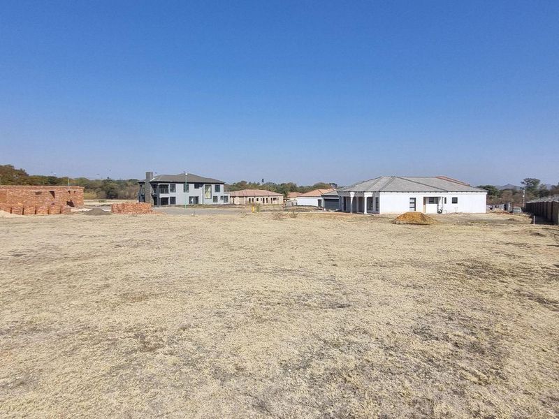 A wide-angle view of a vacant residential plot in a developed estate, featuring cleared land and perimeter fencing with surrounding residential properties.