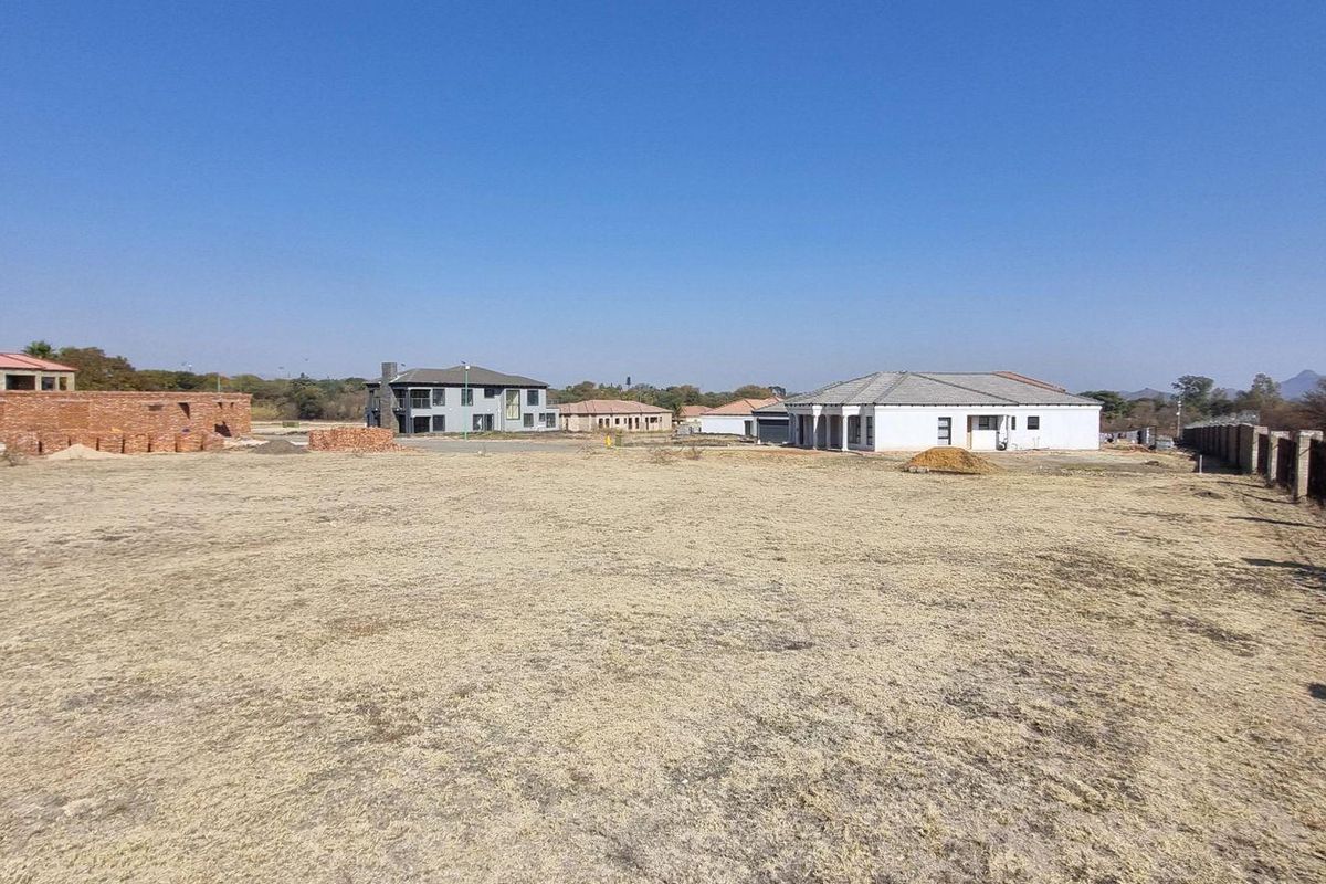 A wide-angle view of a vacant residential plot in a developed estate, featuring cleared land and perimeter fencing with surrounding residential properties.