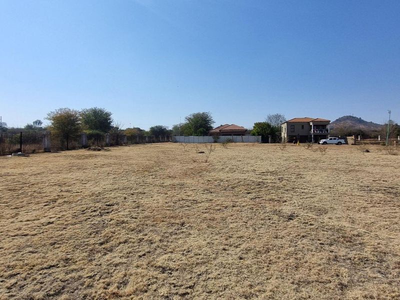 A wide, level vacant residential plot featuring perimeter fencing and clear views of the surrounding neighborhood.