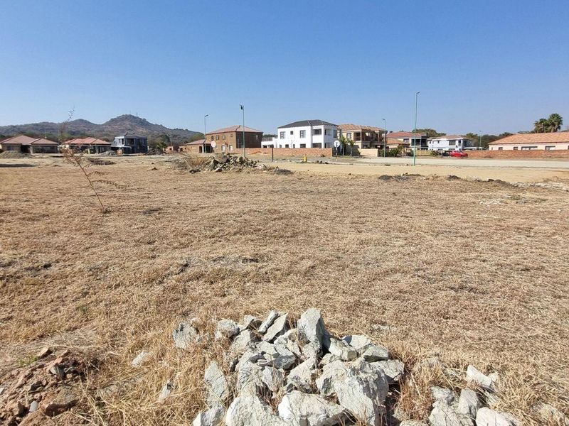 A wide-angle view of a vacant residential plot in a developed estate, featuring dry grass and surrounding suburban housing.
