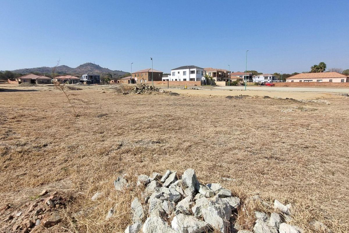 A wide-angle view of a vacant residential plot in a developed estate, featuring dry grass and surrounding suburban housing.