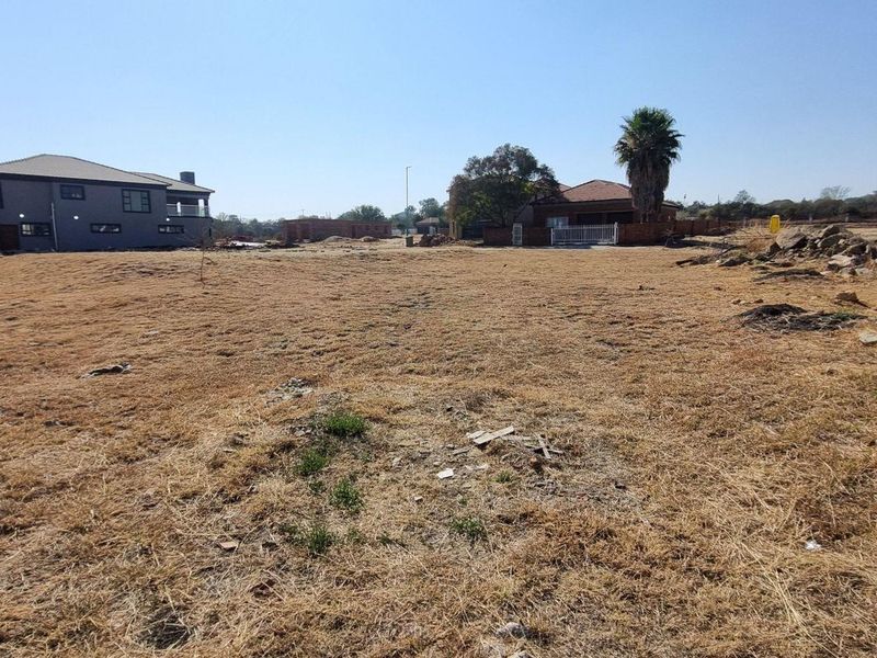 A wide-angle view of a vacant residential plot in a developed estate, showing surrounding homes and clear building potential.