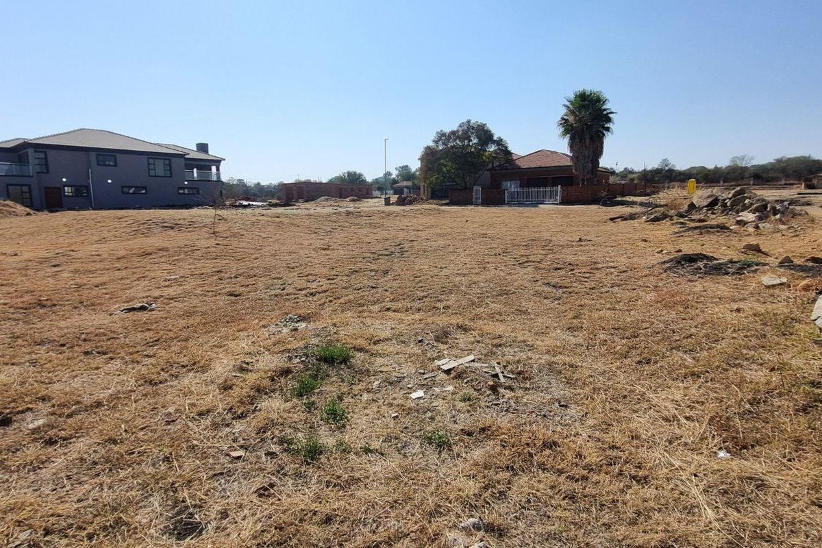 A wide-angle view of a vacant residential plot in a developed estate, showing surrounding homes and clear building potential.