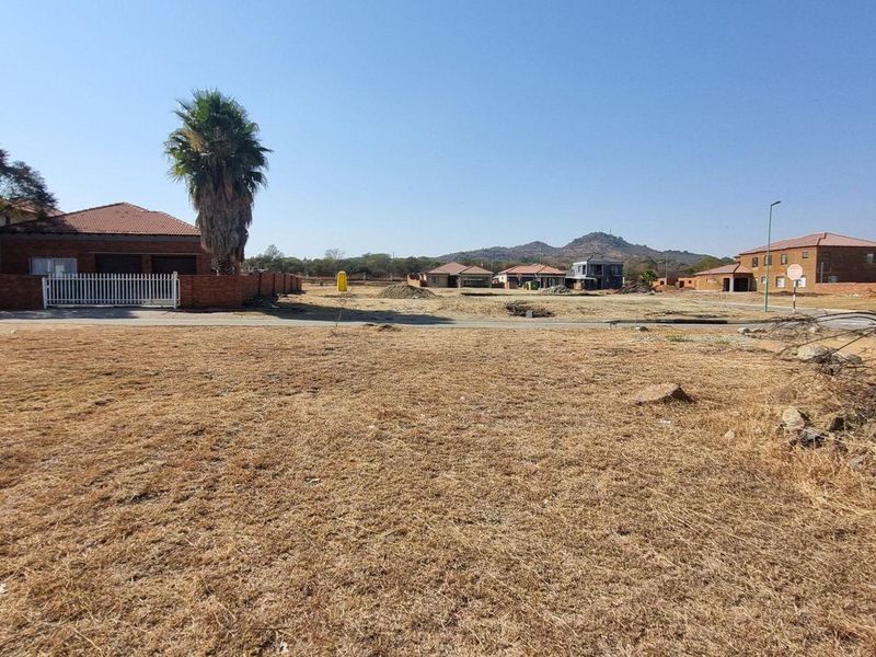 A view of a vacant residential plot in a developed neighborhood, featuring dry grass and surrounding residential infrastructure.