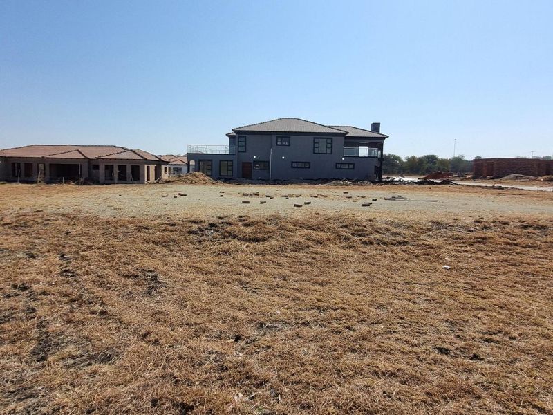 A wide-angle view of a vacant residential plot in a developing estate, showcasing surrounding modern homes and open land.