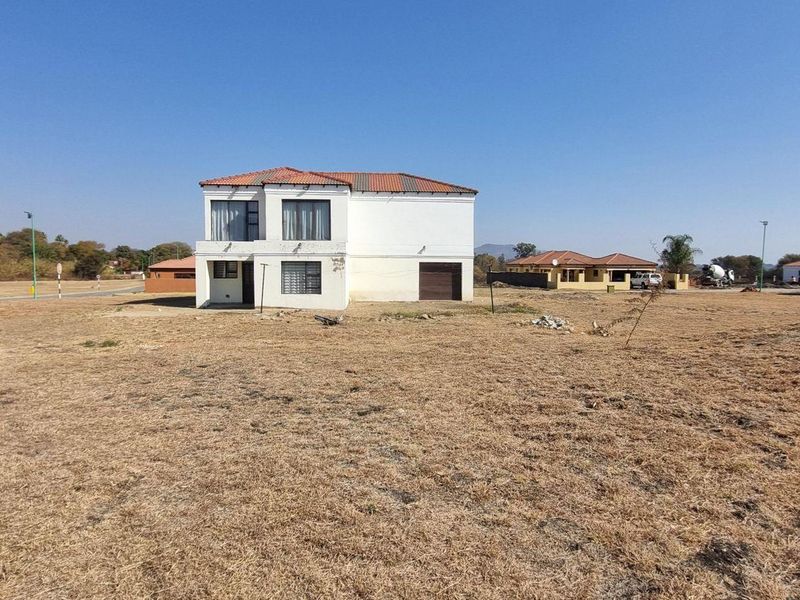 A detached two-story residential property situated on a large, undeveloped plot of land with a tiled roof and garage access.