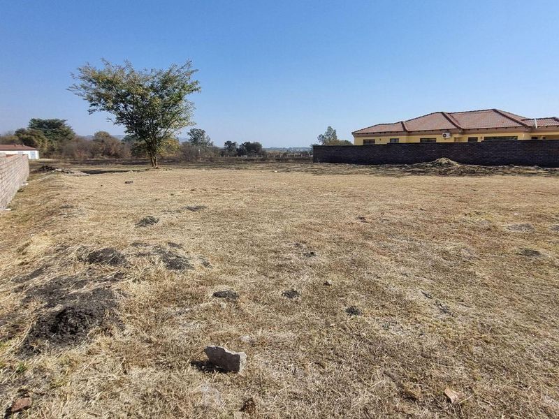 A view of a vacant residential plot featuring a brick boundary wall and open land, suitable for future development.