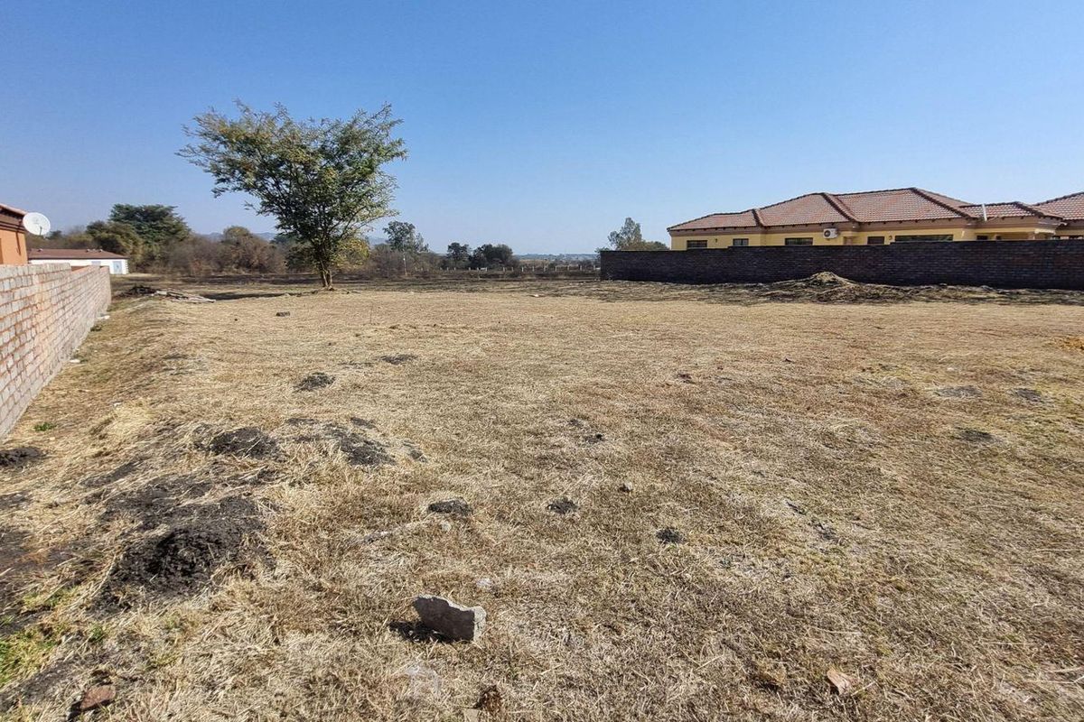 A view of a vacant residential plot featuring a brick boundary wall and open land, suitable for future development.