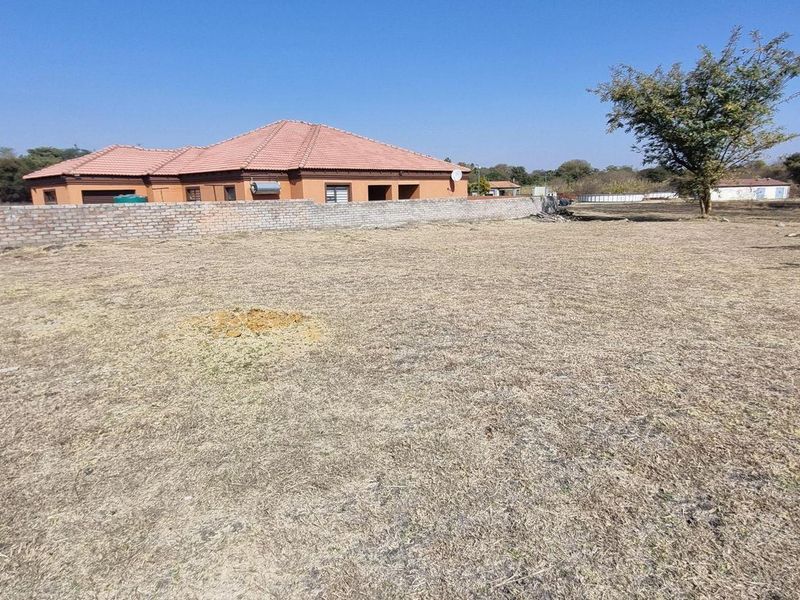 A vacant residential plot featuring a brick boundary wall and a view of the adjacent dwelling with a tiled roof.