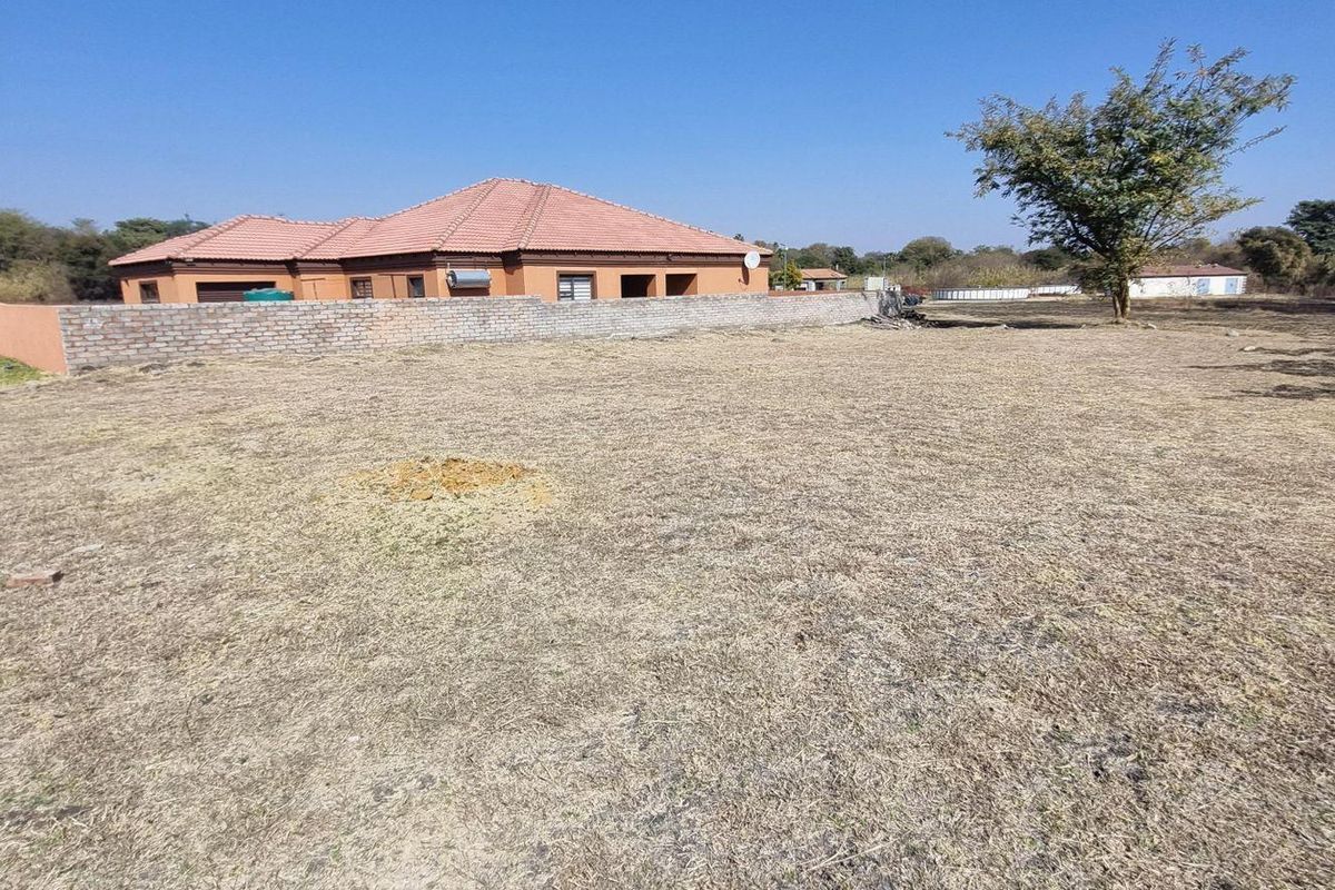A vacant residential plot featuring a brick boundary wall and a view of the adjacent dwelling with a tiled roof.