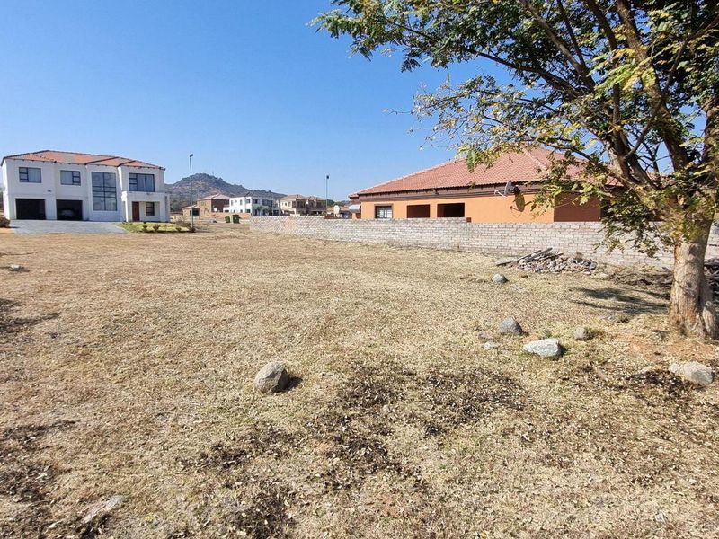 A vacant residential plot featuring dry grass, a mature tree, and a boundary wall, situated in a developed neighborhood.
