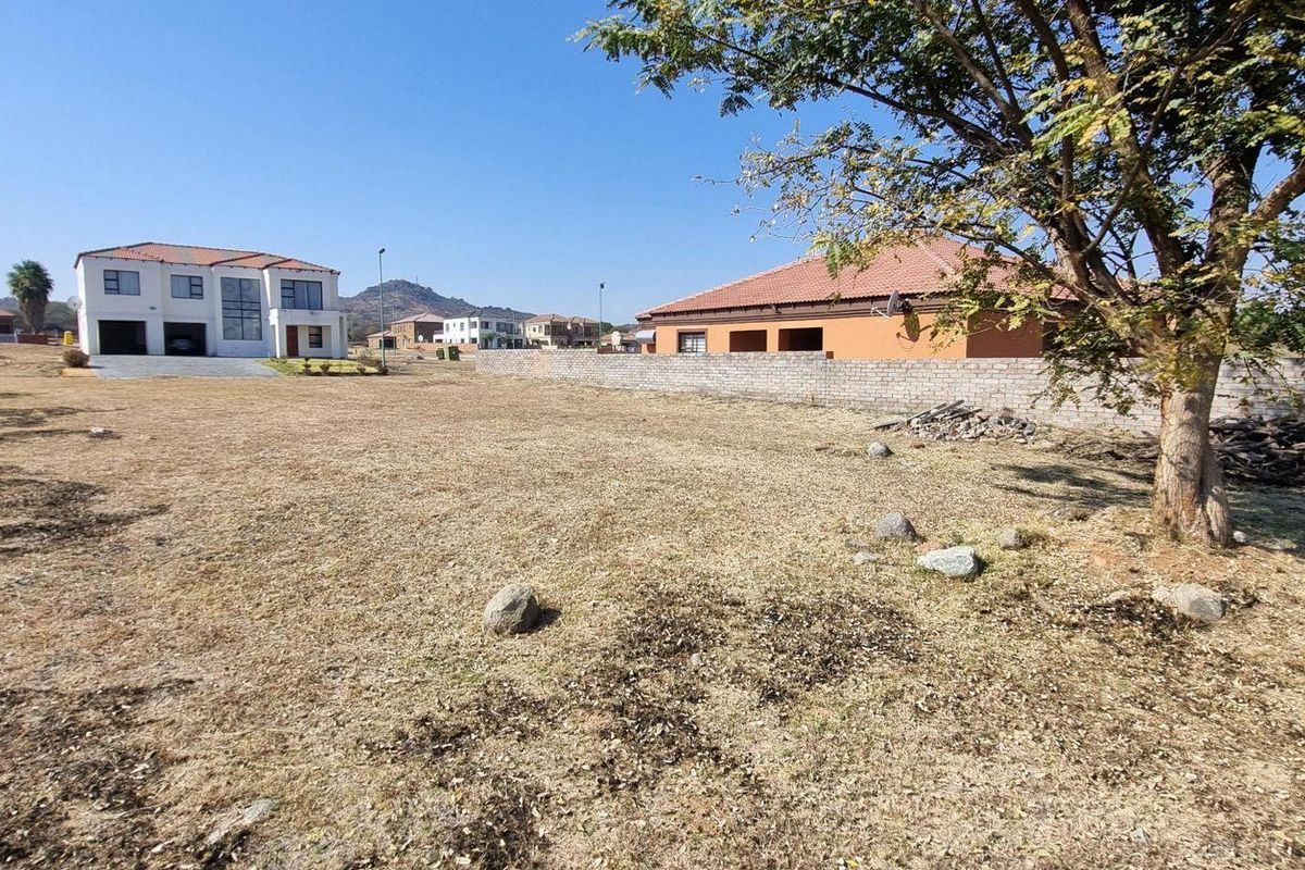 A vacant residential plot featuring dry grass, a mature tree, and a boundary wall, situated in a developed neighborhood.