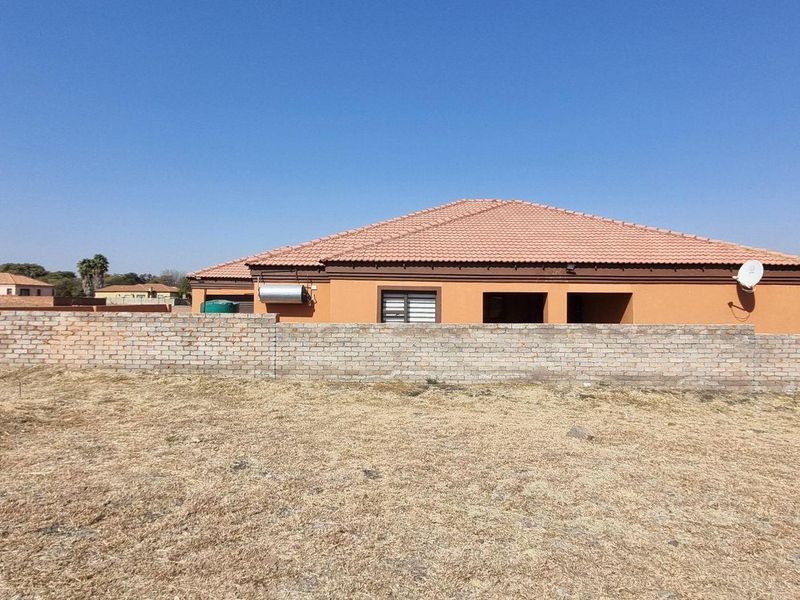 Rear view of a residential property featuring a tiled roof, solar water heater, and a brick boundary wall set on a large plot.