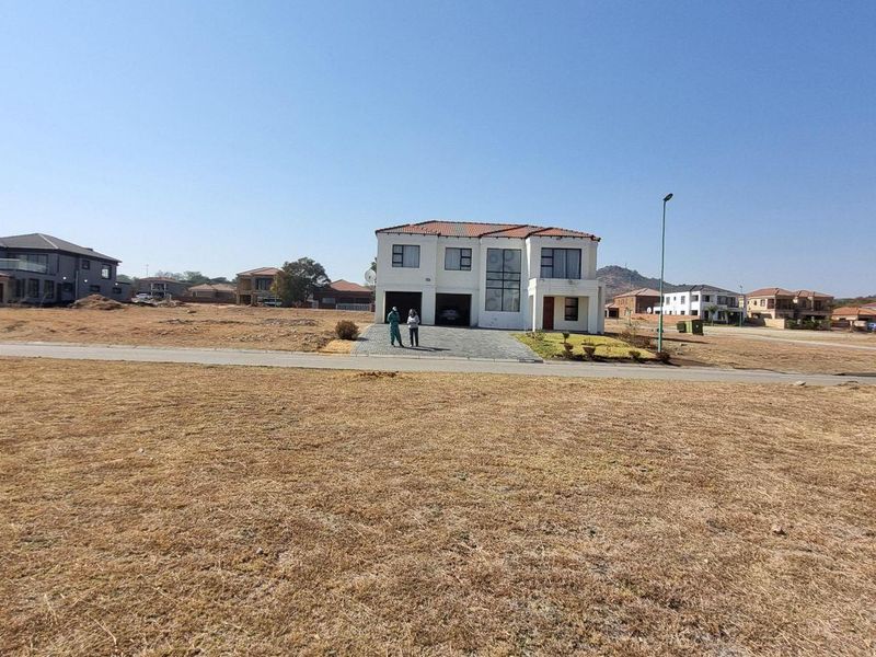 A wide-angle view of a vacant residential plot featuring a paved driveway and a modern two-story house in the background.