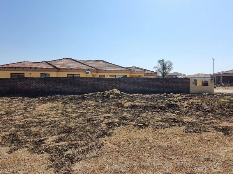 A view of a vacant residential plot featuring a brick boundary wall and a neighboring house in the background.