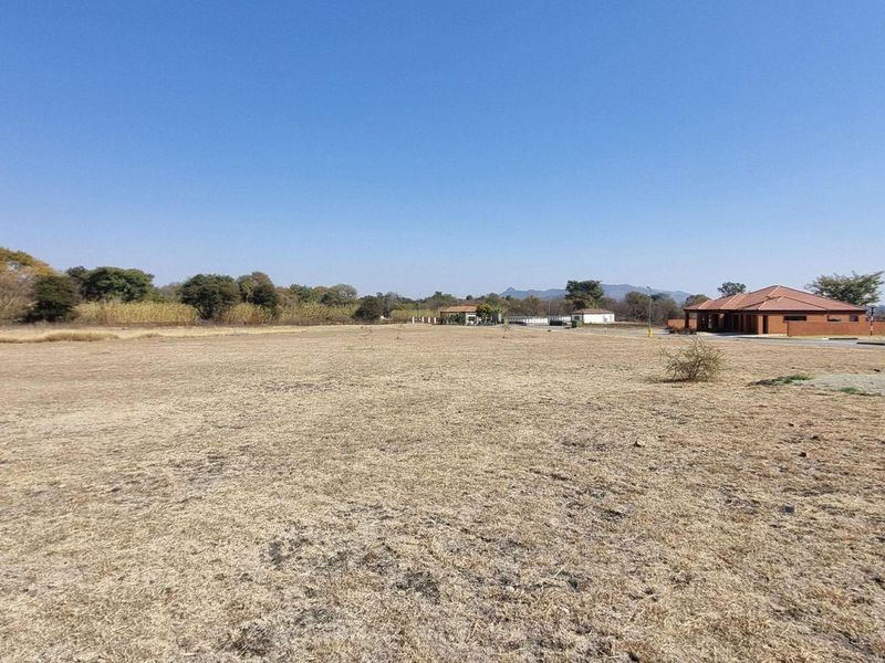 A wide-angle view of a vacant residential plot featuring dry grass, clear skies, and surrounding neighborhood infrastructure.