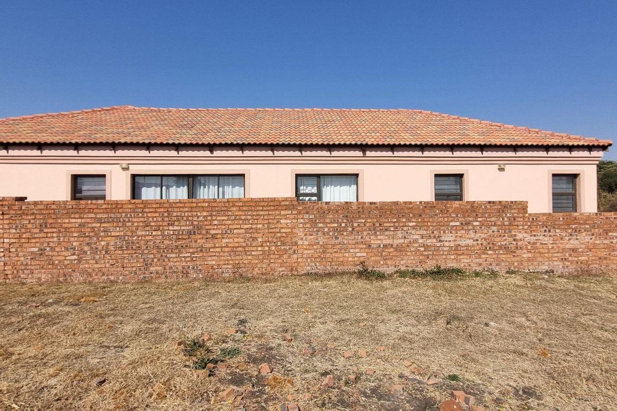 Rear view of a residential property featuring a brick boundary wall, tiled roof, and multiple window and door openings.