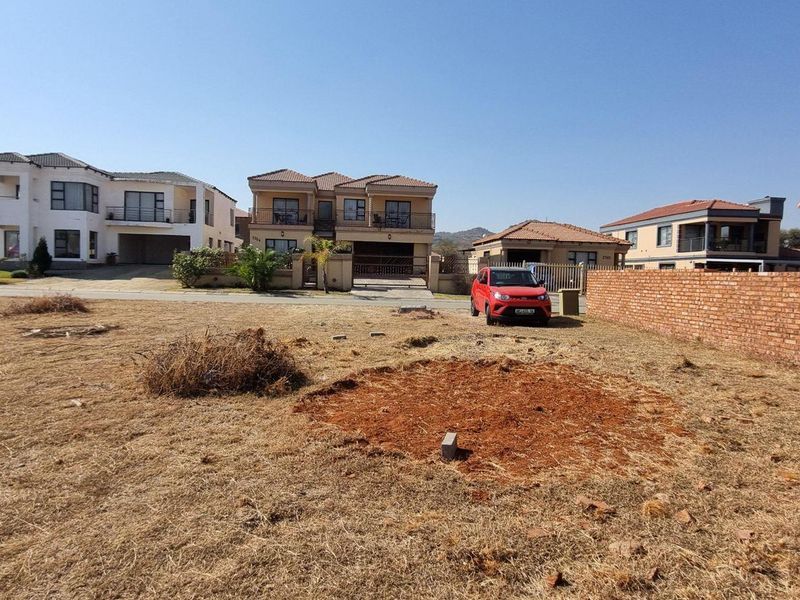 A vacant residential plot featuring a brick boundary wall, situated in a developed neighborhood with surrounding residential homes.