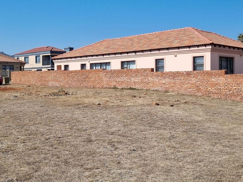 A vacant residential plot featuring a brick boundary wall, situated in a developed neighborhood setting.