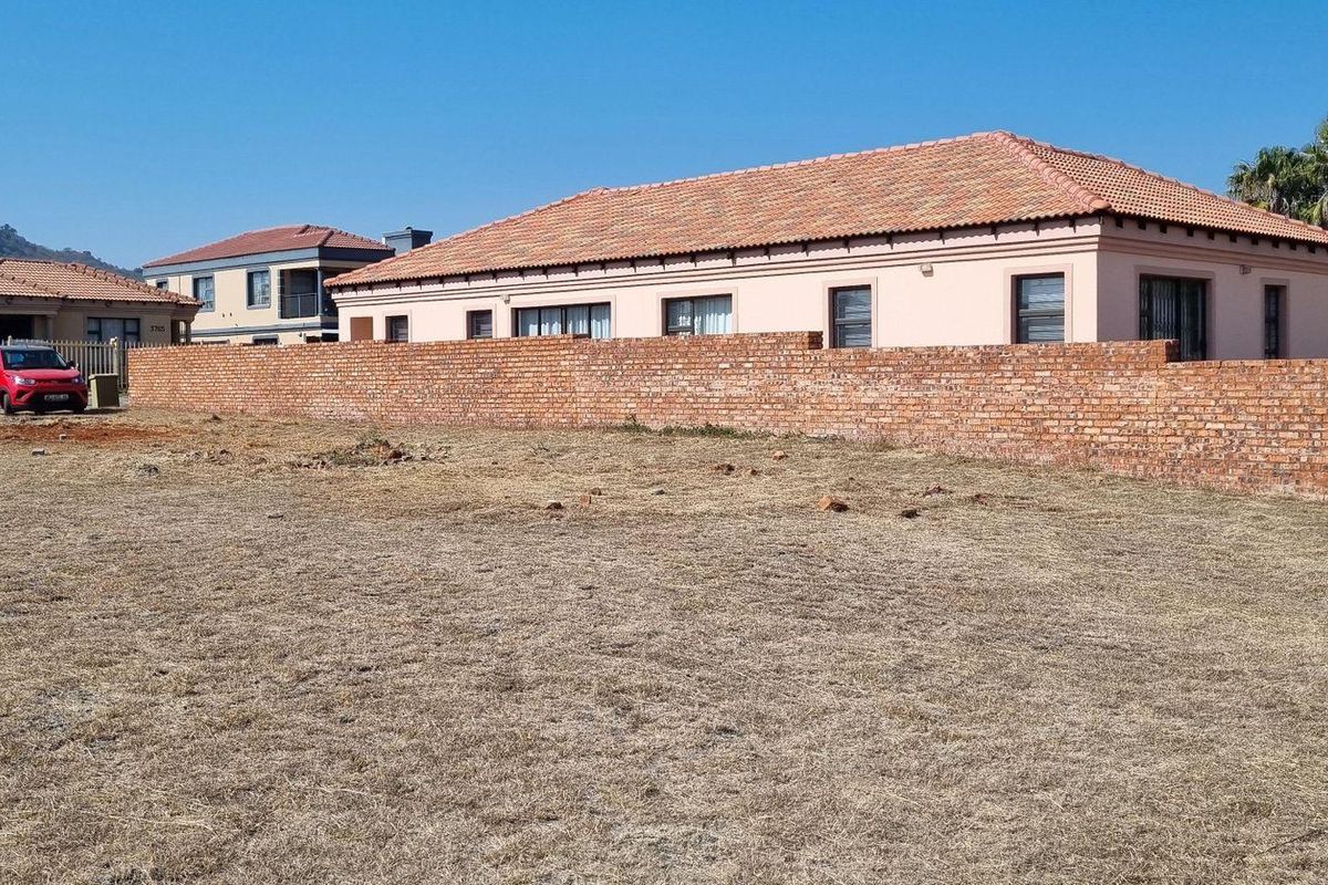 A vacant residential plot featuring a brick boundary wall, situated in a developed neighborhood setting.