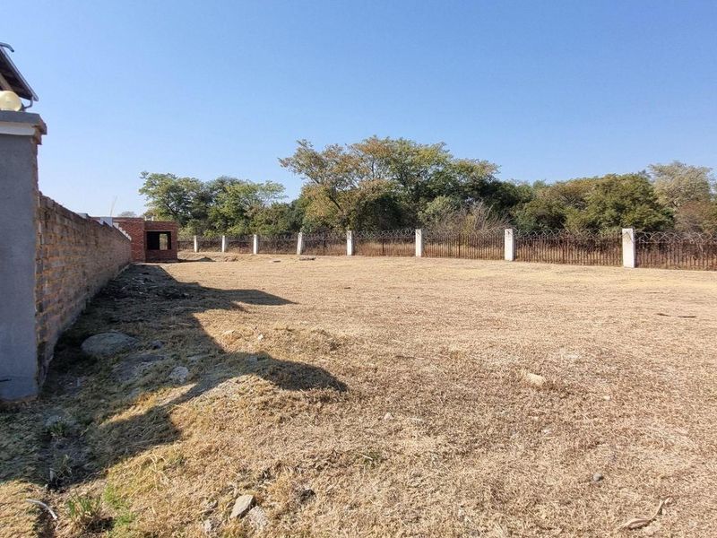A spacious, level backyard area featuring a perimeter wall with security fencing and established trees along the rear boundary.