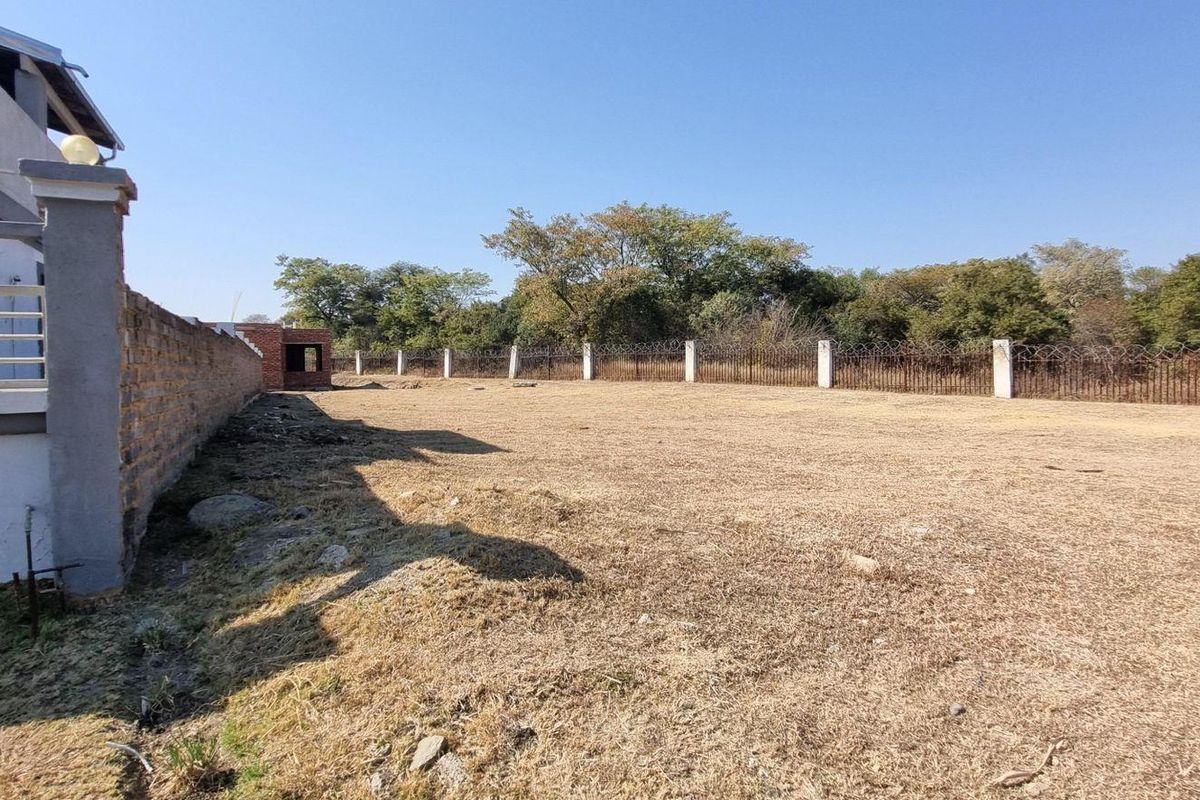 A spacious, level backyard area featuring a perimeter wall with security fencing and established trees along the rear boundary.