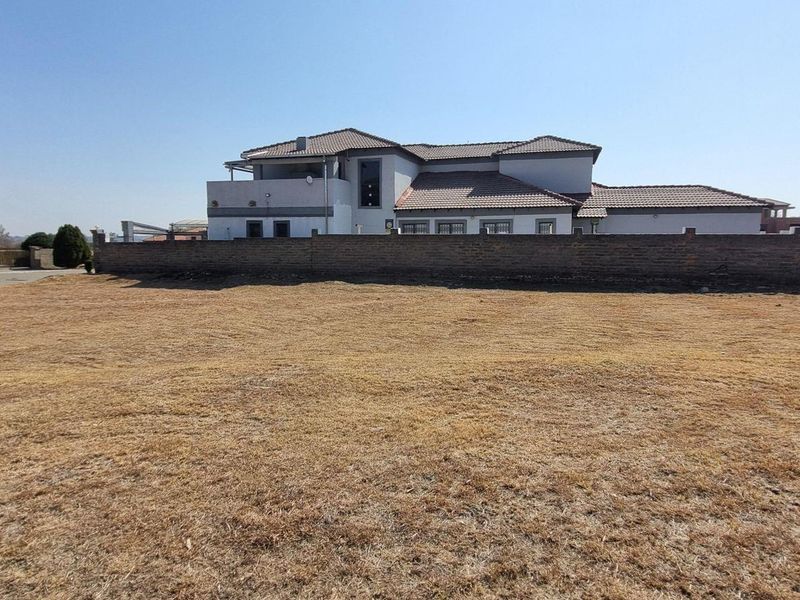A view of a vacant residential plot with a boundary wall and neighboring property in the background.