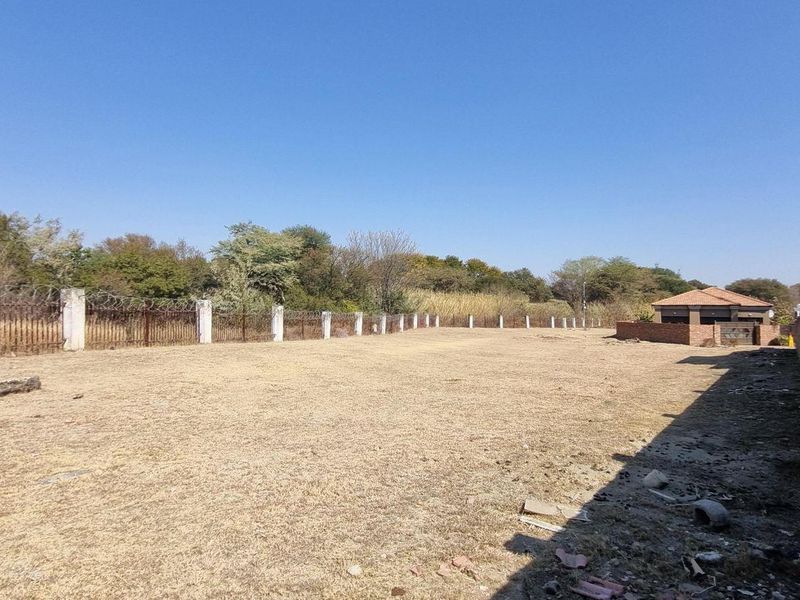 A vacant residential plot featuring perimeter fencing with razor wire and a concrete boundary wall, offering a clear space for potential development.
