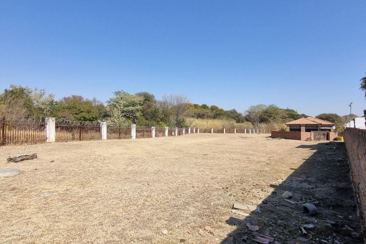 A vacant residential plot featuring perimeter fencing with razor wire and a concrete boundary wall, offering a clear space for potential development.