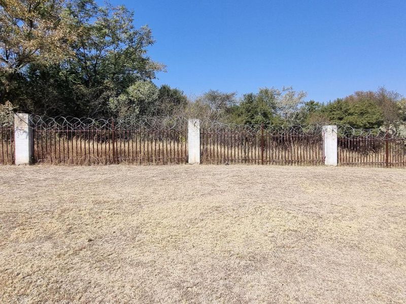 A vacant residential plot featuring dry grass and a perimeter fence with integrated razor wire and concrete support posts.