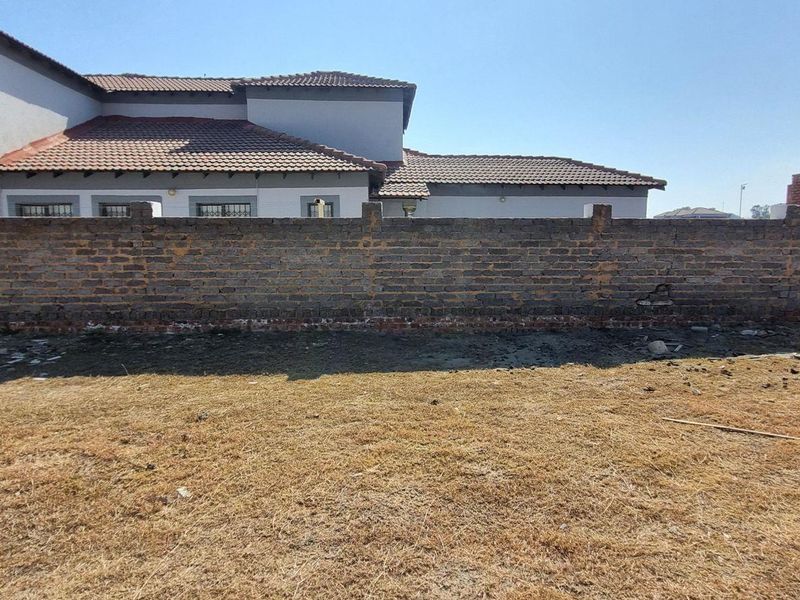 A view of a vacant residential plot featuring a weathered brick boundary wall and adjacent residential property with a tiled roof.