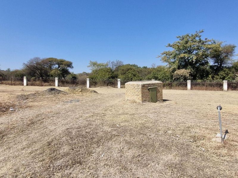 A view of the vacant residential land featuring a perimeter fence, dry grass, and a small brick utility structure.