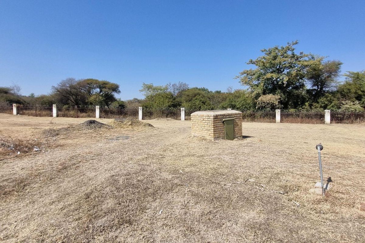 A view of the vacant residential land featuring a perimeter fence, dry grass, and a small brick utility structure.
