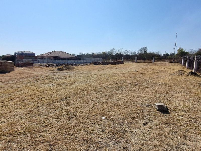 A vacant residential plot featuring perimeter fencing with razor wire, offering a clear space ready for development in a residential estate.