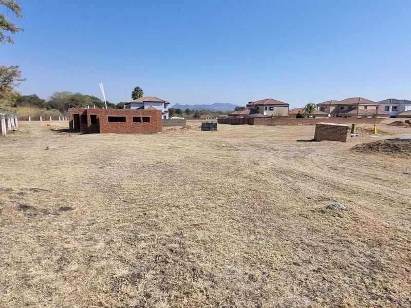 A vacant residential plot featuring perimeter fencing with razor wire and a partially constructed brick building structure on site.