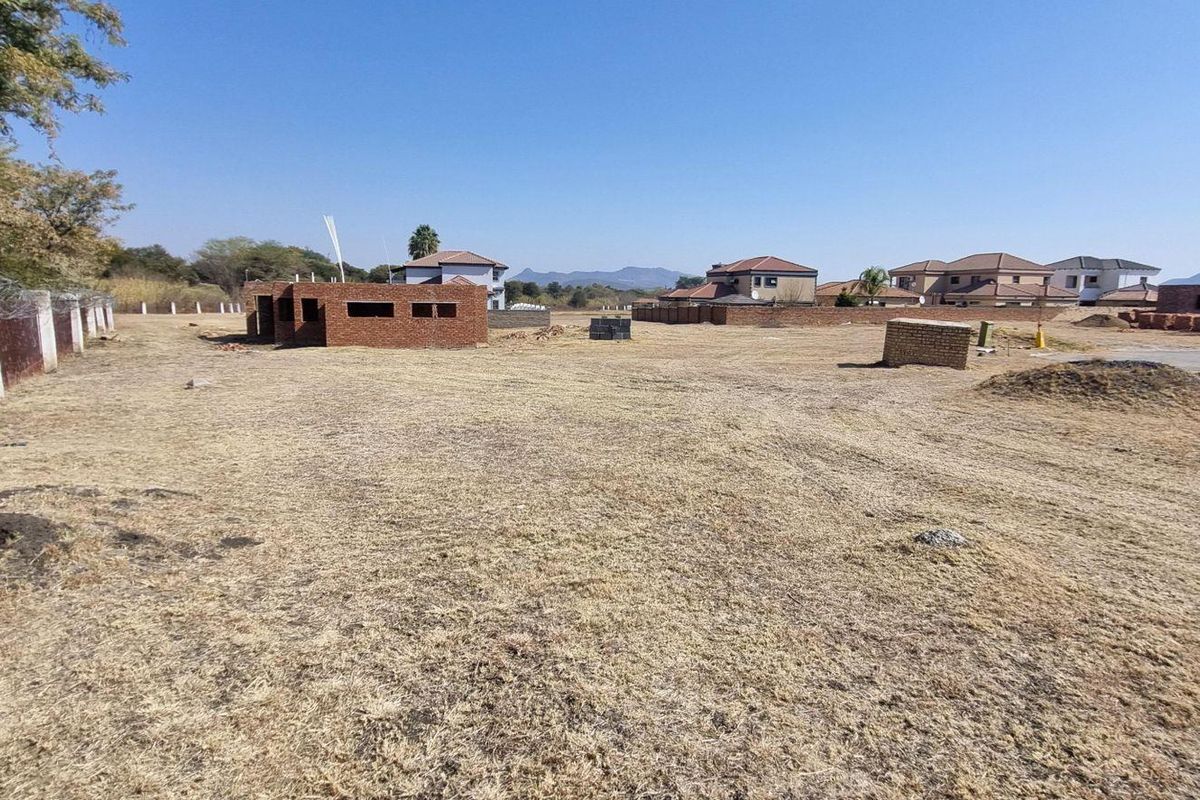 A vacant residential plot featuring perimeter fencing with razor wire and a partially constructed brick building structure on site.